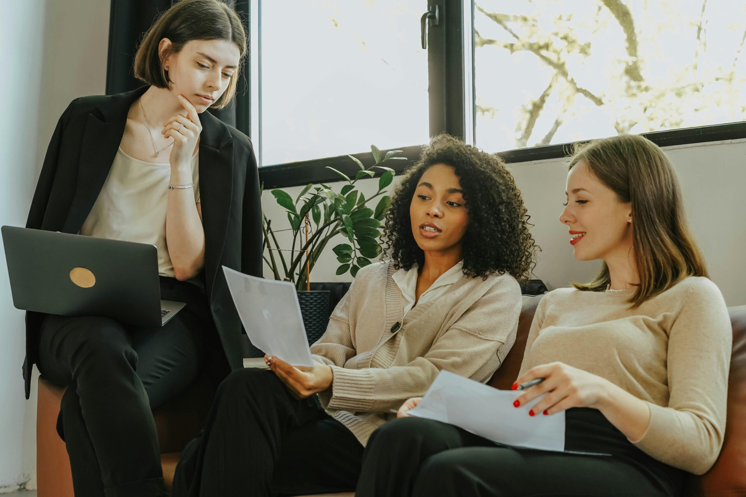 Three women in business casual clothing looking over a paper together