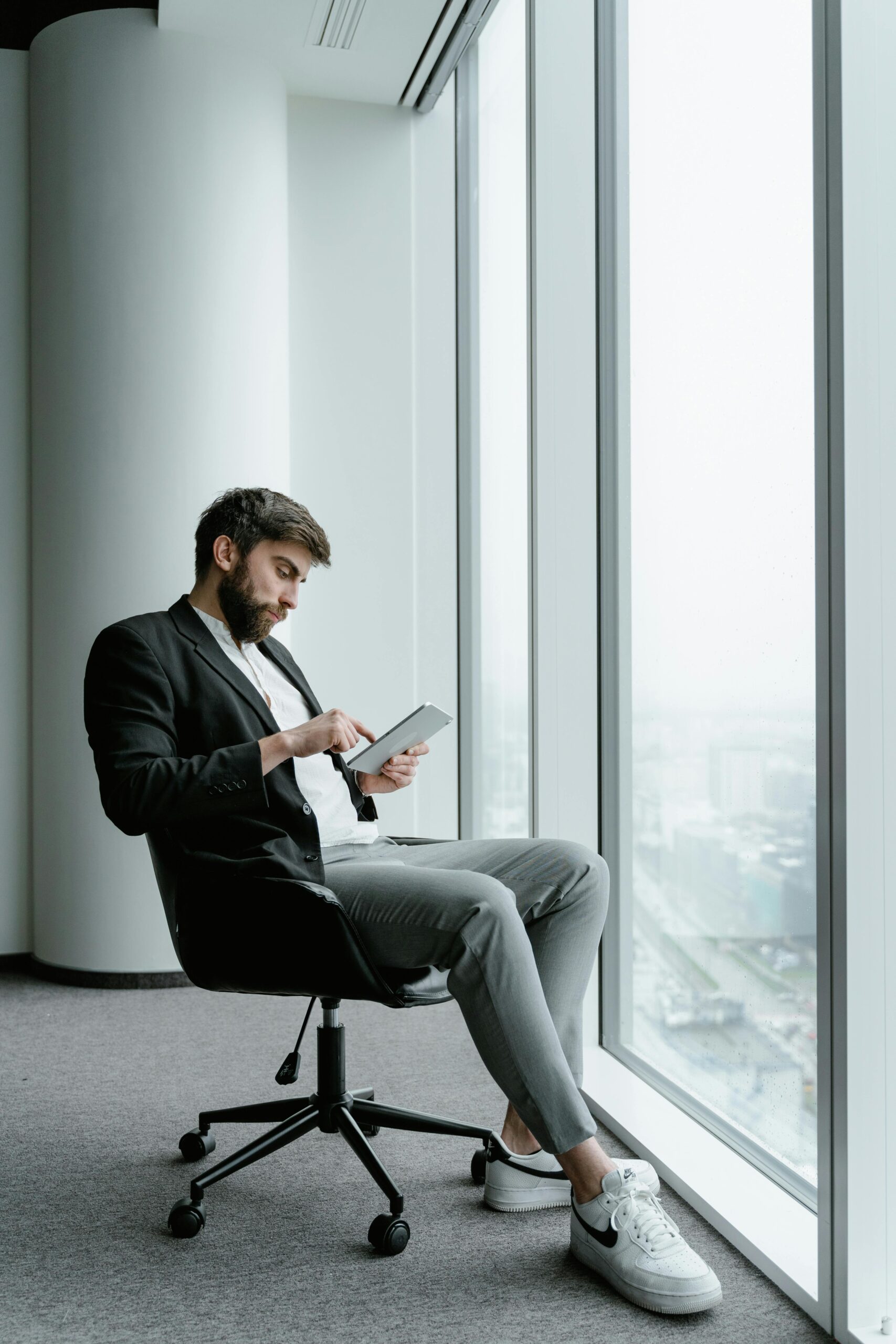 man in business attire sitting next to window on tablet
