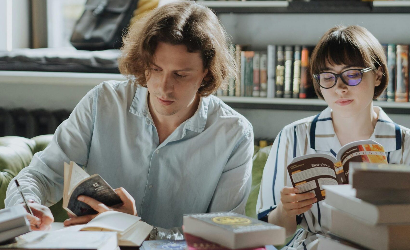 two students reading with piles of books in front of them