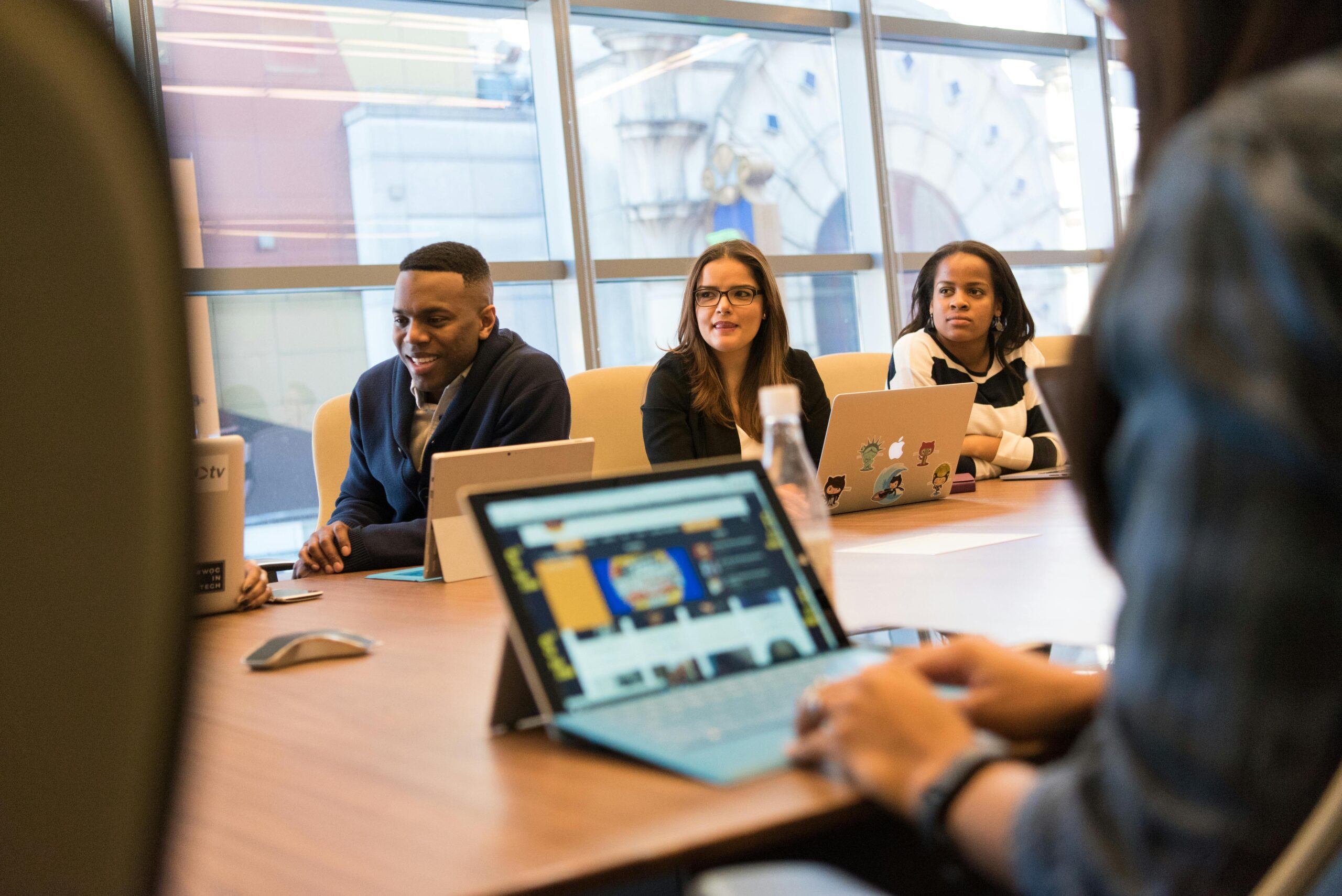 Group of people in business attire sitting around a conference table with laptops