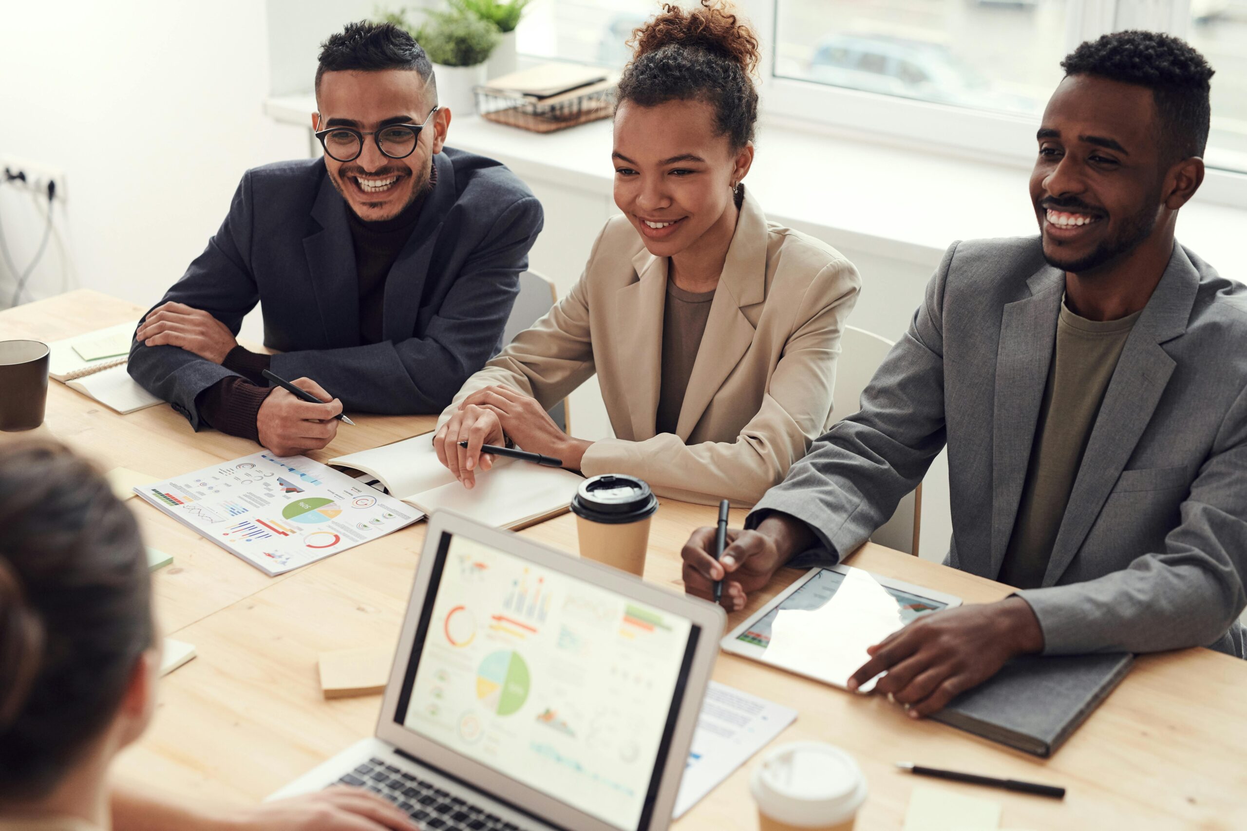 Three people dressed in business attire at a conference table amongst papers and laptops
