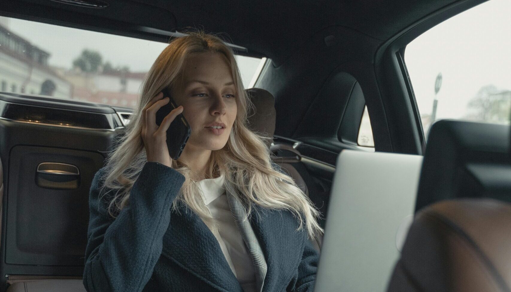 Business woman on phone in back of town car looking at laptop