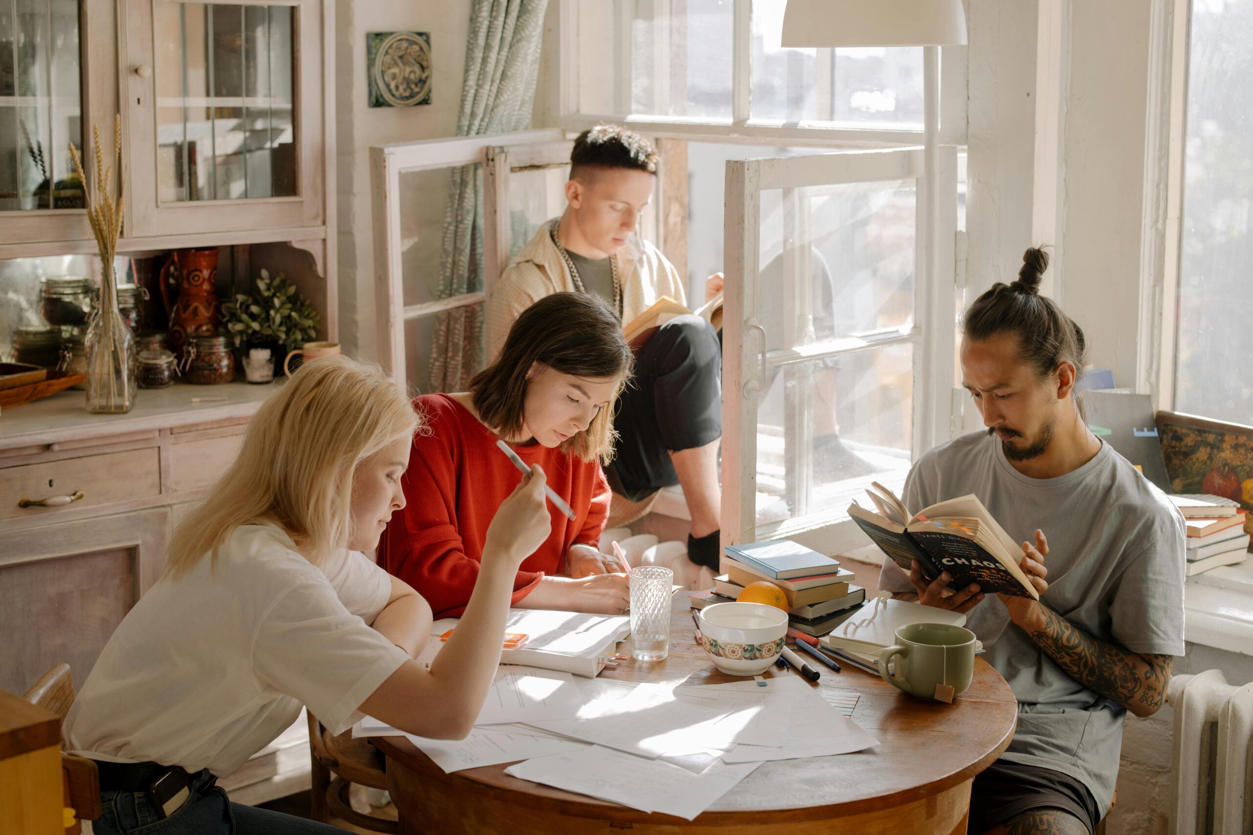Four college-aged students studying at kitchen table with natural sunlight coming in through window