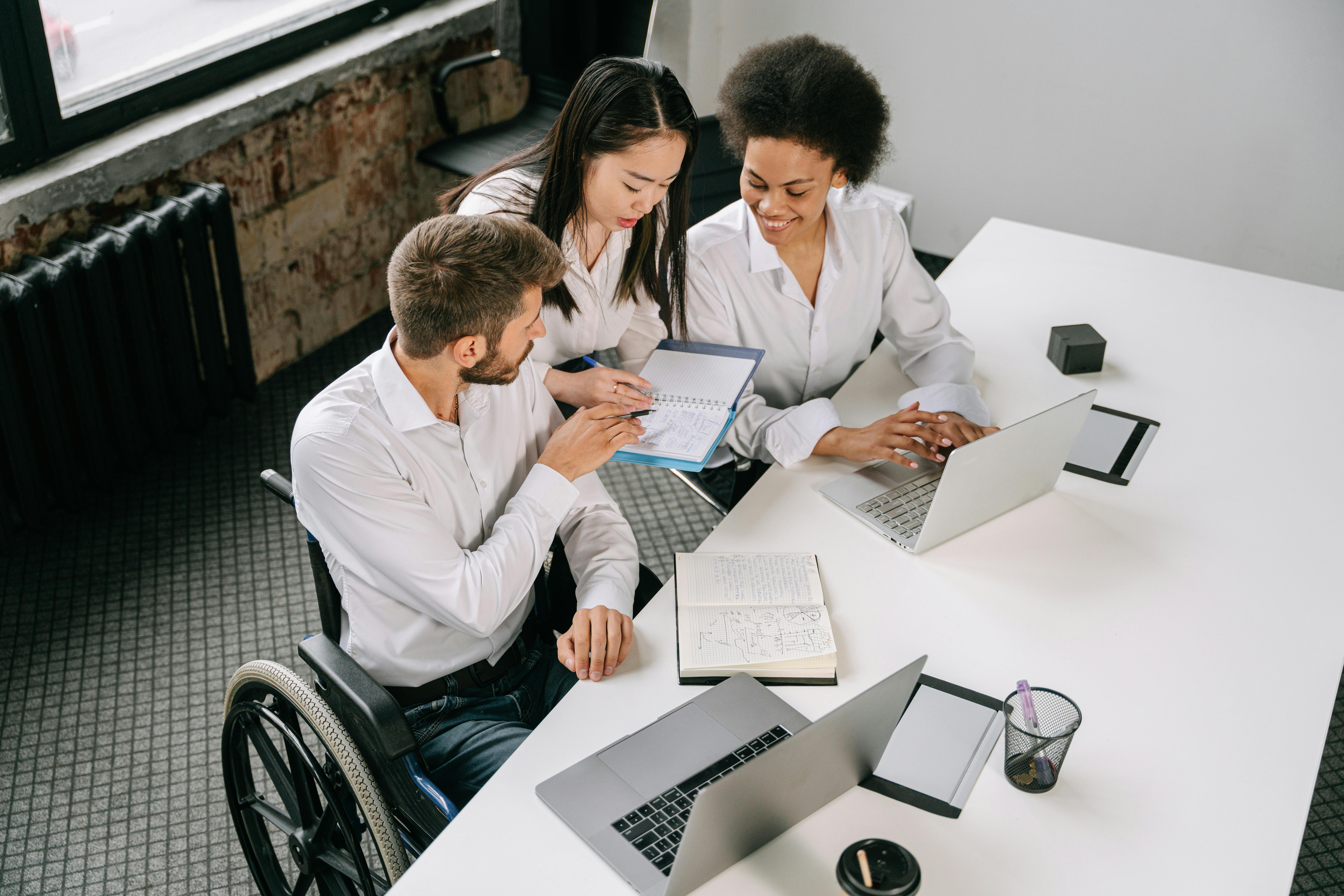 Business man sitting in wheelchair going over information with two women in business attire