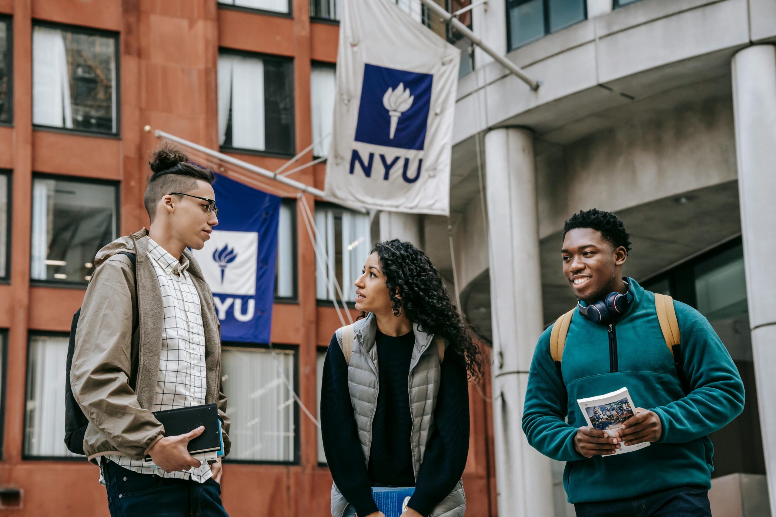 Three students standing underneath NYU flags
