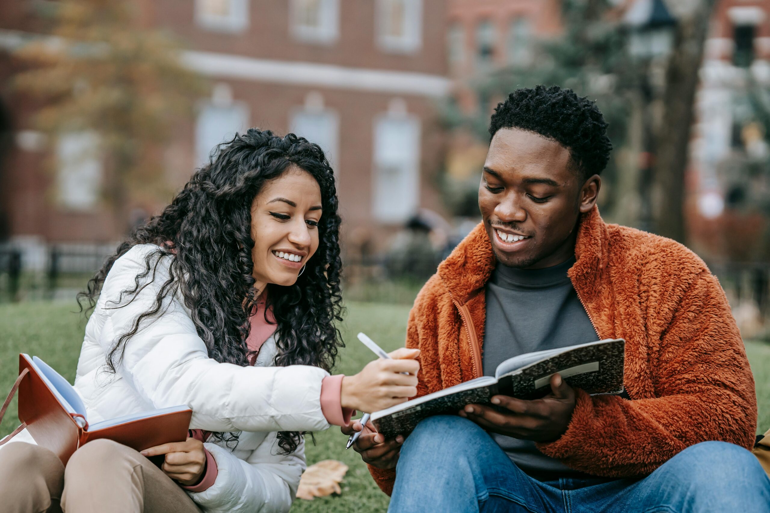 Two students sitting in university lawn looking at notebook
