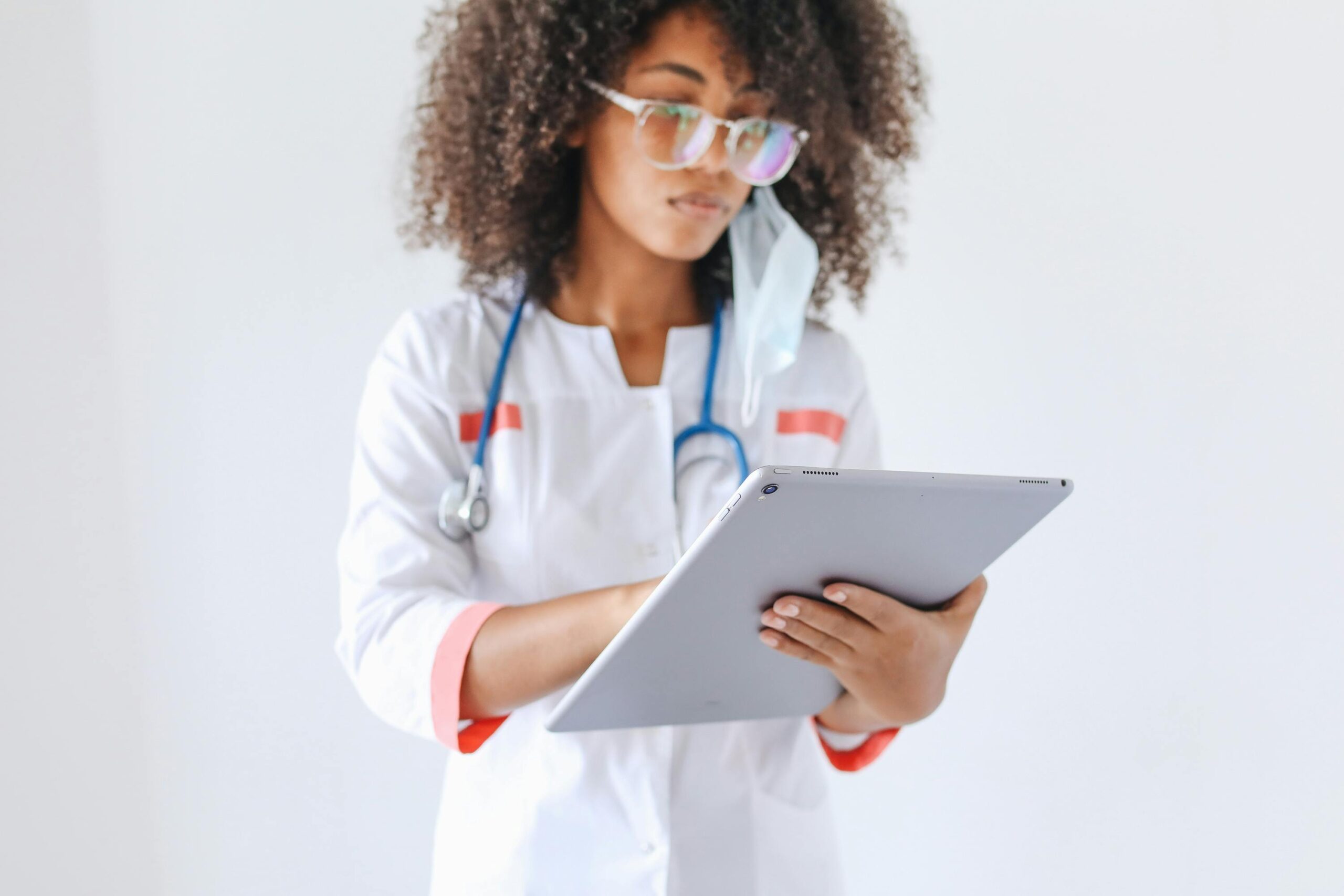 A young female doctor wearing a stethoscope reviews a patient's prescription on her tablet.