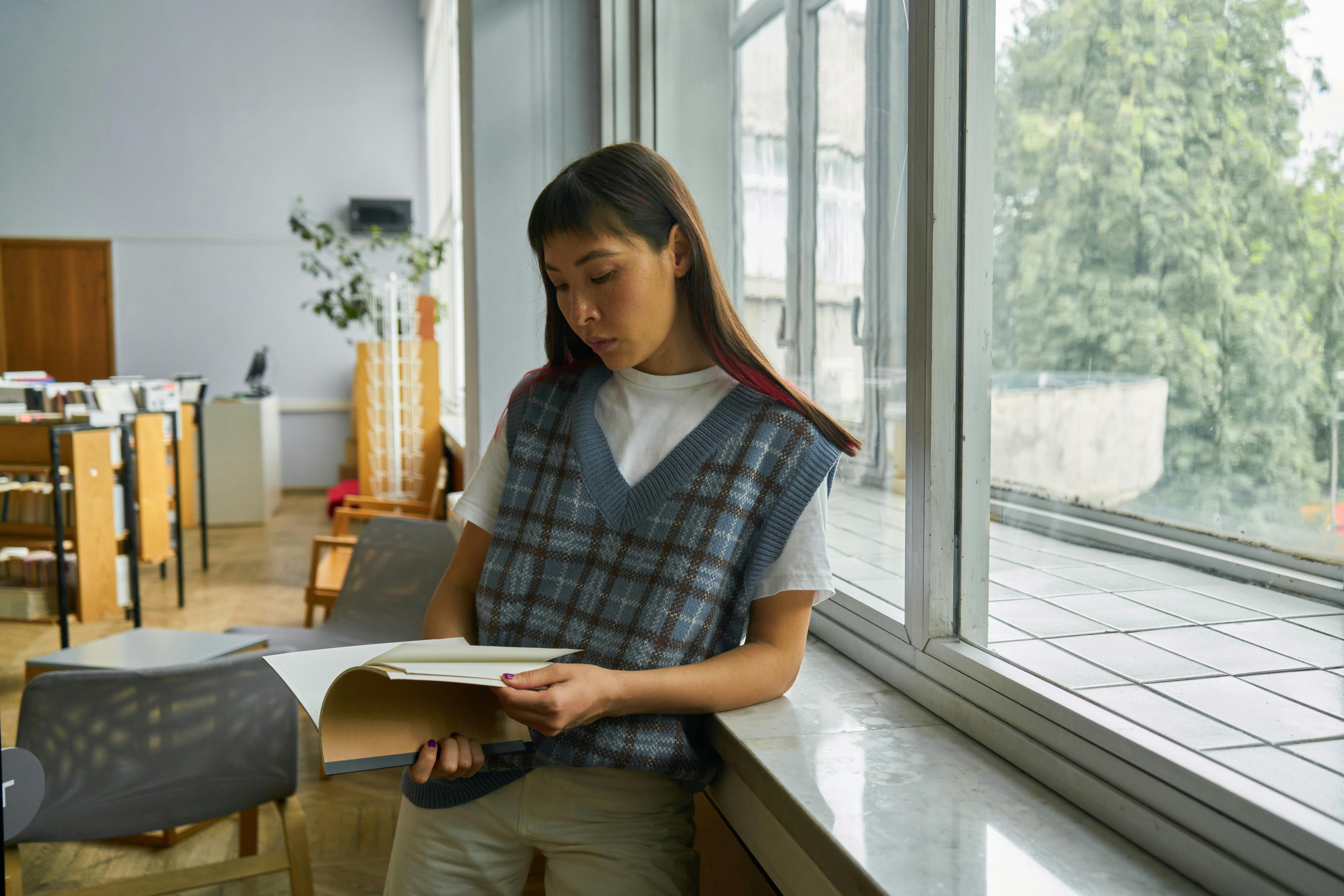 Woman reading a Book while leaning on a Window Pane