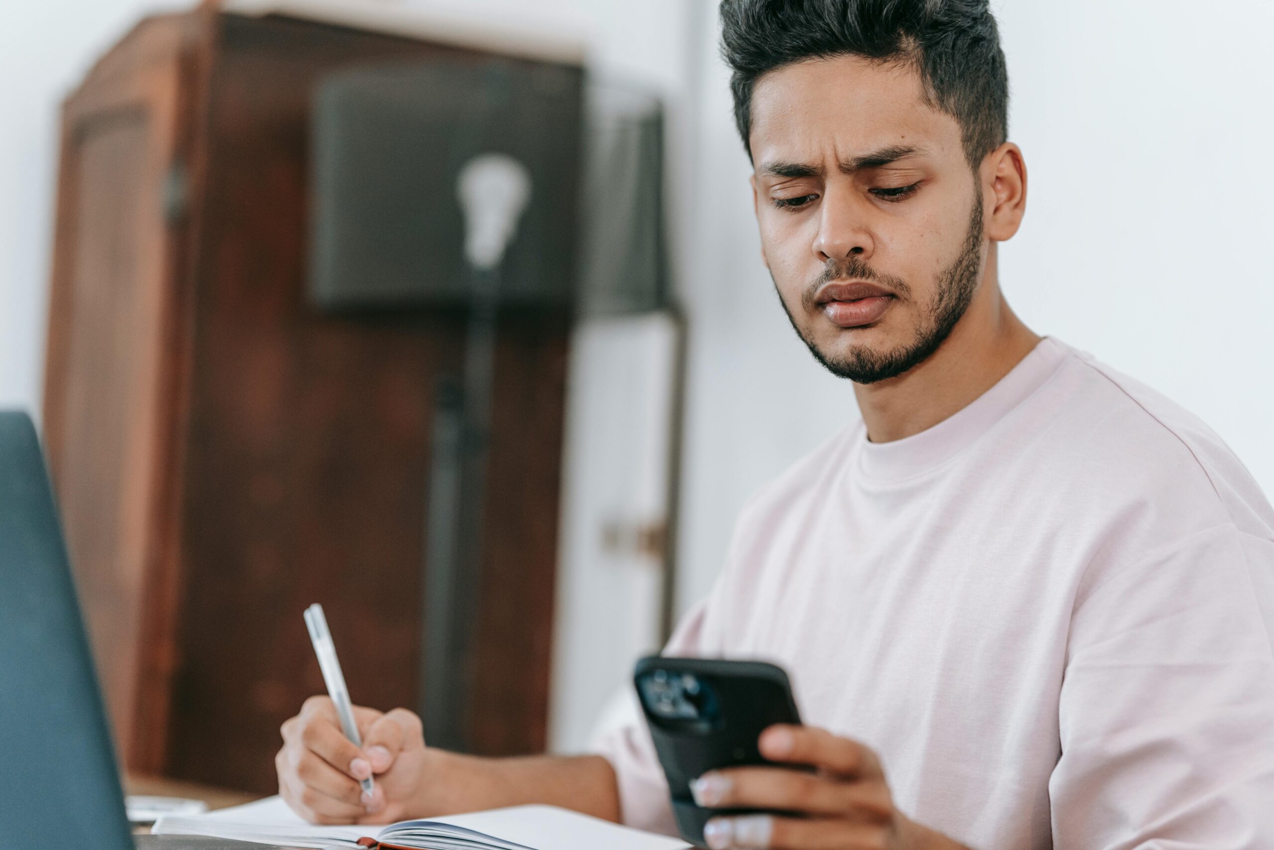 Serious ethnic man using smartphone and working on laptop