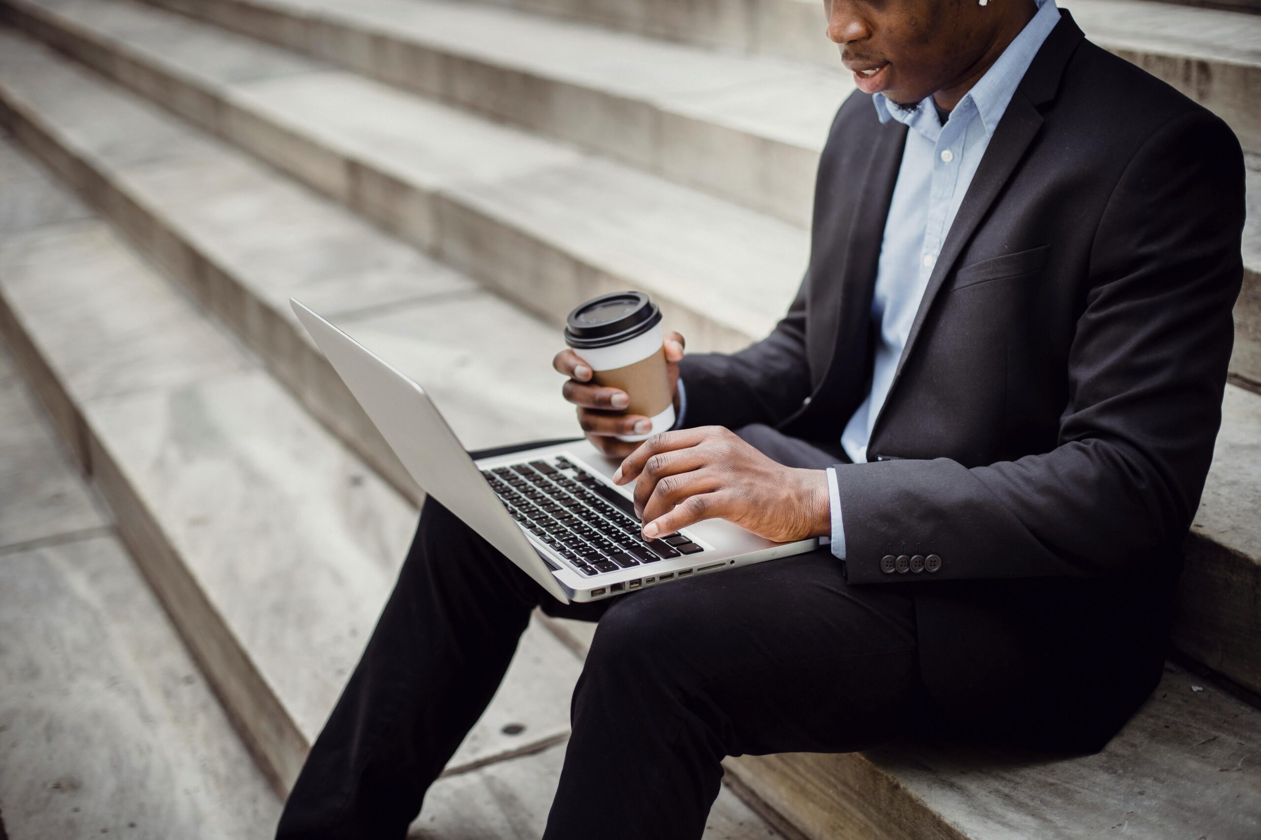 Crop cheerful black businessman using laptop on street stairs